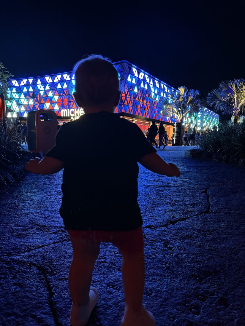 A small child walking toward a building covered in colored lights at night