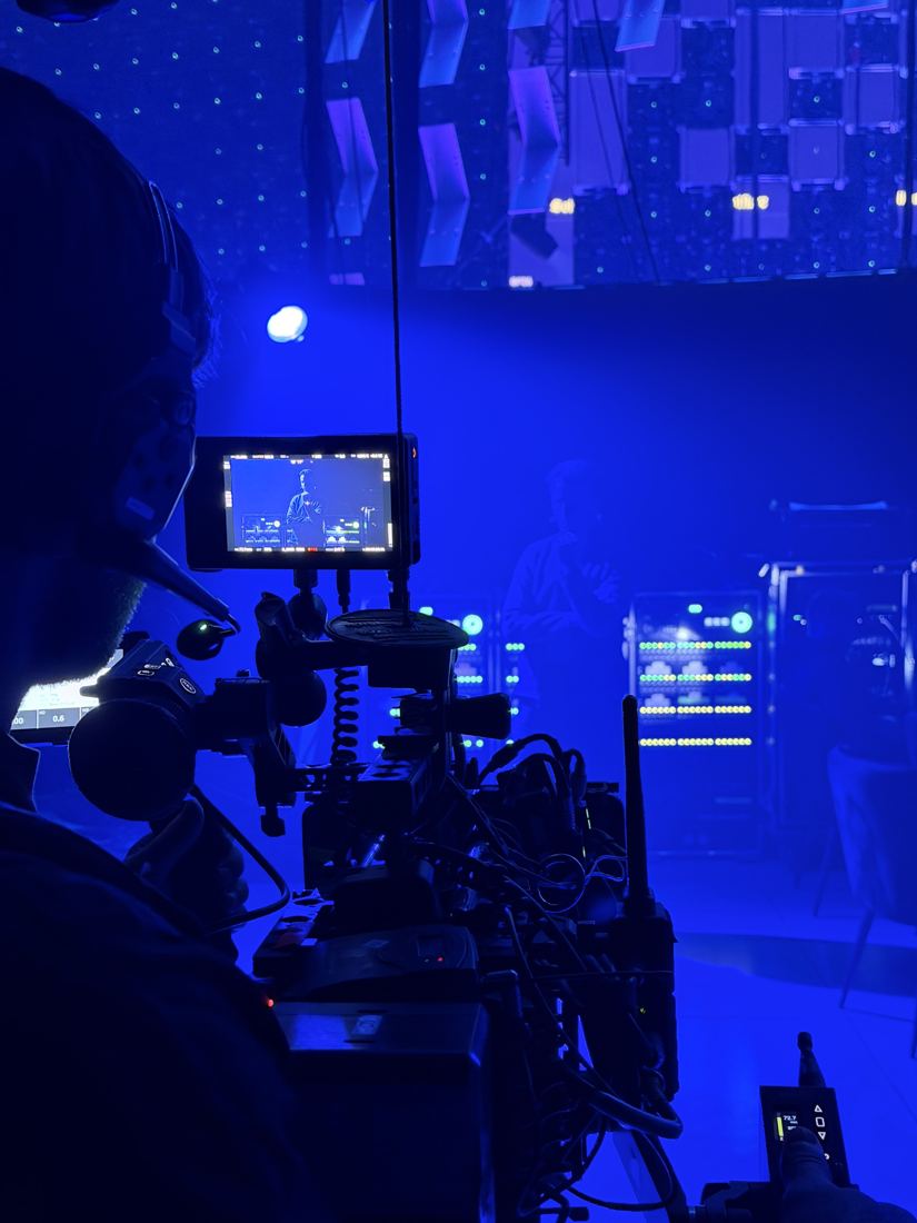 Camera operator filming a speaker on a blue-lit set