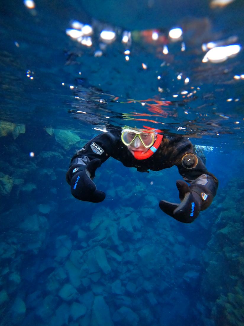 Snorkeler in a drysuit in very clear blue water