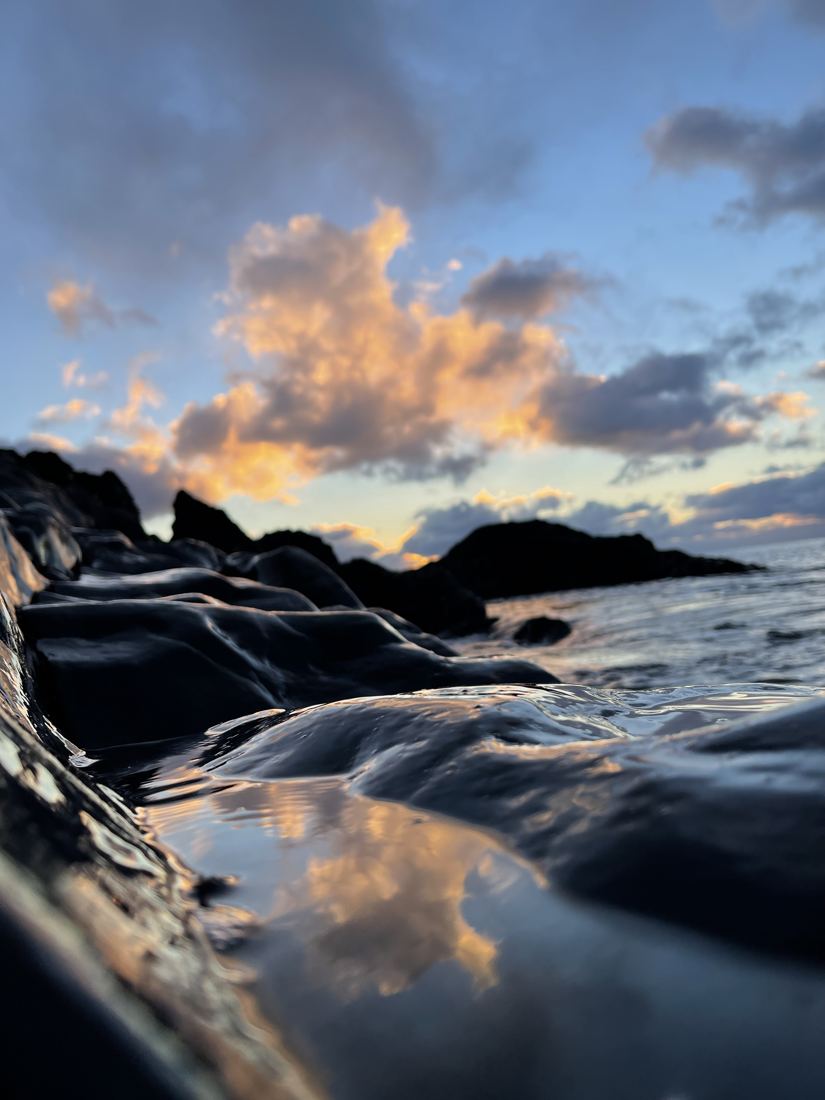 Wet black rock at water level with clouds lit at sunset